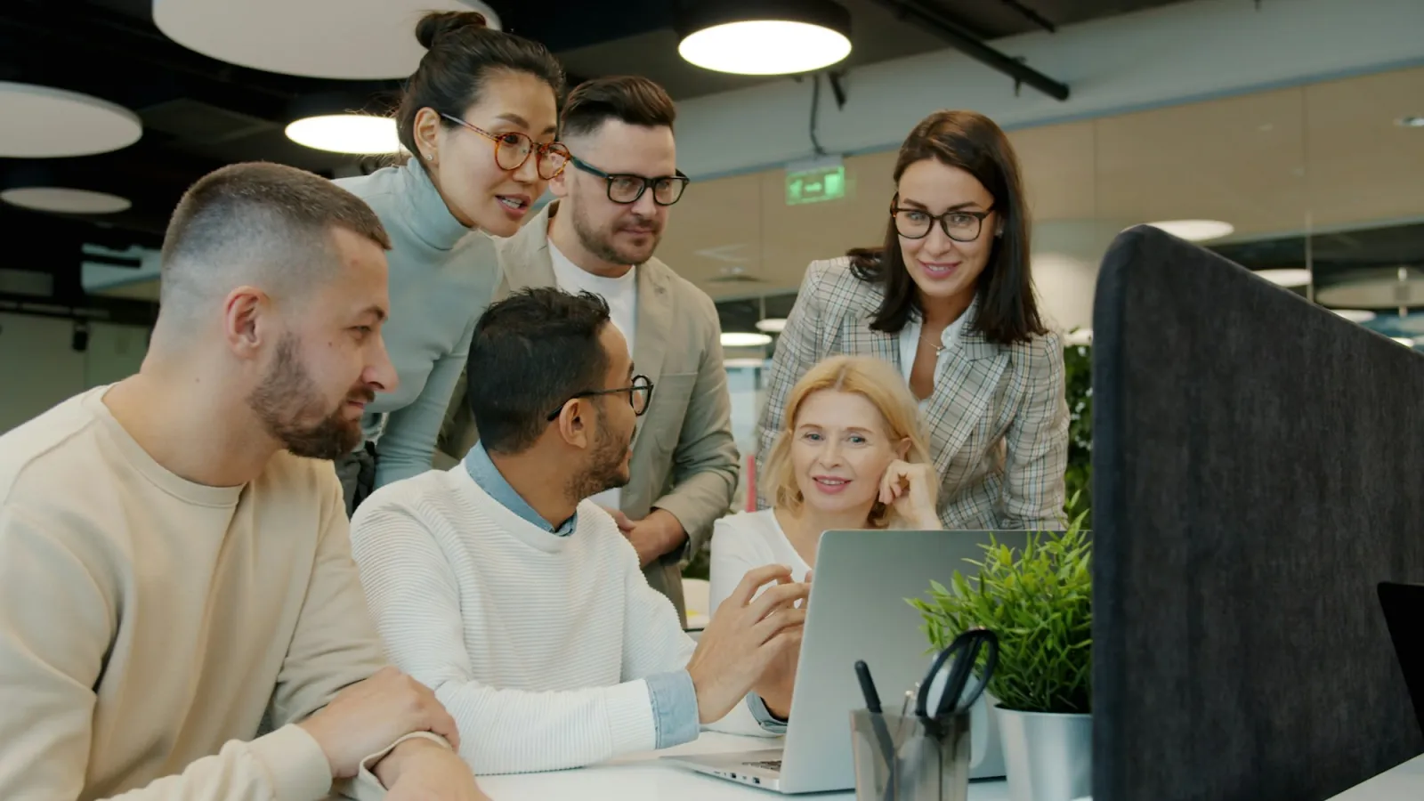 A small team gathered around a laptop, one colleague walking the others through something on screen